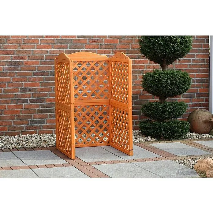 Promadino Mülltonnenbox Verkleidung Rex - 78,5 x 86,5 x 128 cm, Honigbraun - Eine dekorative, orangefarbene Sichtschutzwand aus Holz mit einem eleganten Gittermuster im Garten, die Privatsphäre und Schutz bietet.