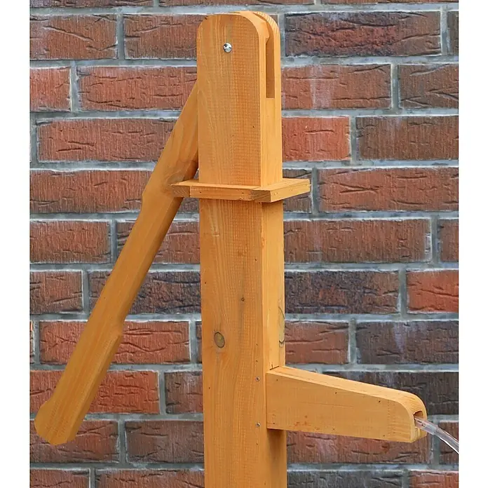Promadino Standbrunnen - Ø x H: 64 x 101 cm, Solarpumpe - Eine hölzerne Wasserpumpe im Freien vor einer Ziegelwand. Die Pumpe ist aus hellem Holz gefertigt und funktionsbereit.