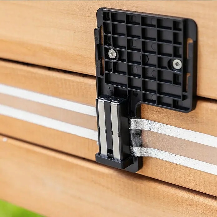 Windhager Schneckenzaun E-Fence - 10 m, Batteriebetrieben - Nahaufnahme eines Holzrahmens mit einem schwarzen Kunststoffverbinder, der mit zwei Schrauben befestigt ist und ein silbernes Metallband hält.