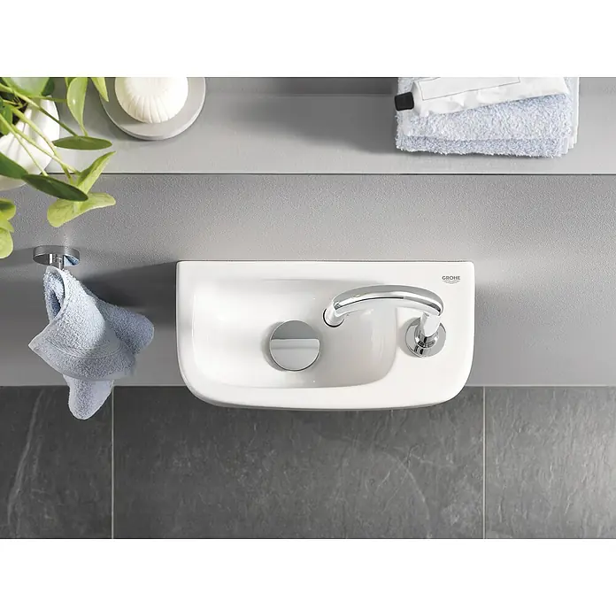Grohe Kaltwasser-Standventil Universal - C-Auslauf, Chrom, Glänzend - Draufsicht auf ein kleines, modernes Waschbecken mit Armatur und Handtuchhalter in einem stilvollen Badezimmer.
