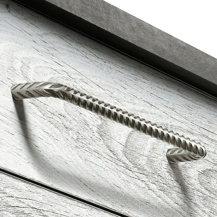 Häfele Tirador para muebles 117.30.316 - L x An x Al: 17,25 x 4 x 1,6 cm, Acero - Primer plano de un tirador de metal con un diseño detallado en un mueble de madera clara.
