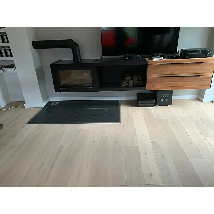 Fertigparkett - Eiche Weiß, 1.900 x 190 x 14 mm, Landhausdiele - Ein modernes Wohnzimmer mit einem schwarzen Kamin und einem Holzregal an der Wand. Der helle Holzboden sorgt für eine freundliche Atmosphäre.