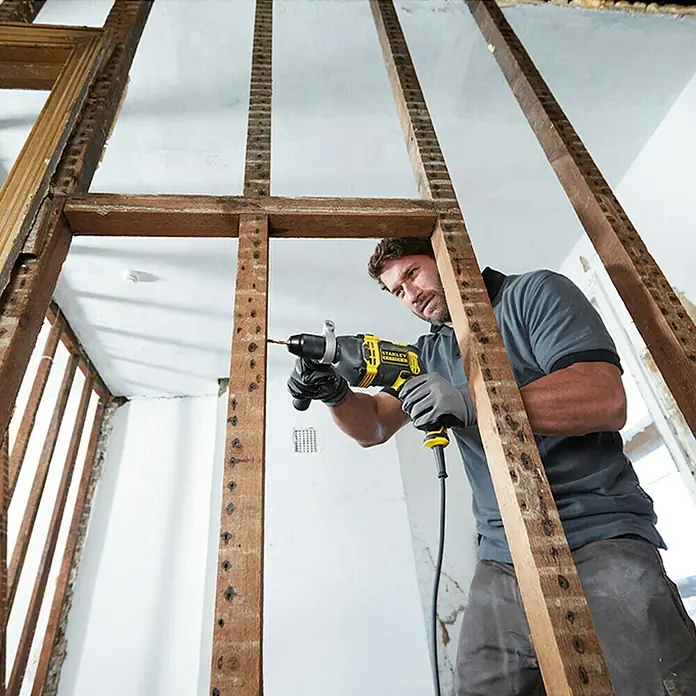 Stanley FatMax Taladro percutor FMEH850K-QS - 850 W, Portabrocas de sujeción rápida - Artesano perforando una pared de madera con un taladro percutor amarillo STANLEY.