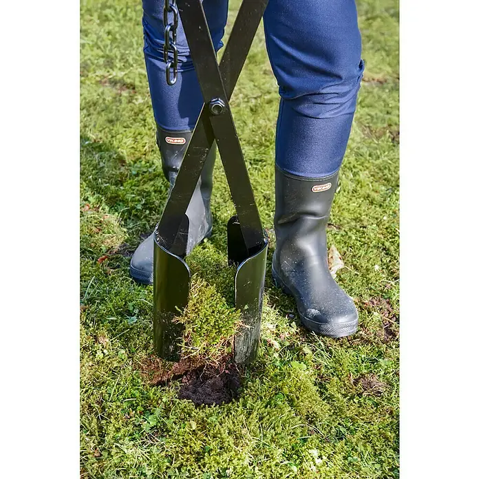 Gardol Handbagger - Länge: 150 cm, Material Stiel: Eschenholz - Erdlochstecher in Aktion. Das Werkzeug sticht ein Loch in den Rasen, während eine Person mit Gummistiefeln daneben steht. Praktisches Gartengerät!