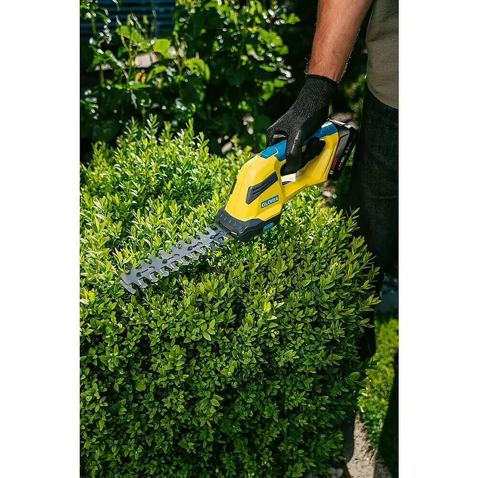 Gloria Power for All 18V Akku-Gras- & Strauchschere FineCut 18V compact - 18 V, Li-Ionen, Ohne Akku, Schnittbreite: 14 cm - Nahaufnahme einer Gloria-Heckenschere beim Schneiden einer Hecke, ideal für präzise Gartenarbeit.