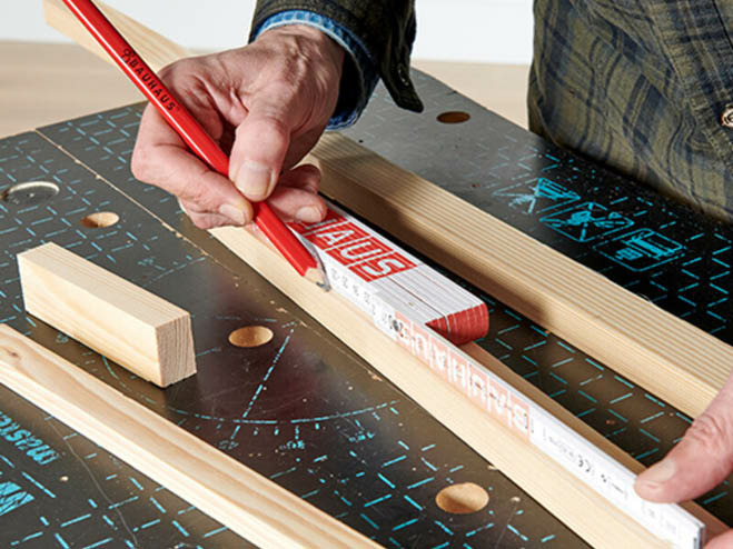 Mit Zollstock und Bleistift wird eine Markierung auf einer Rechteckleiste gesetzt