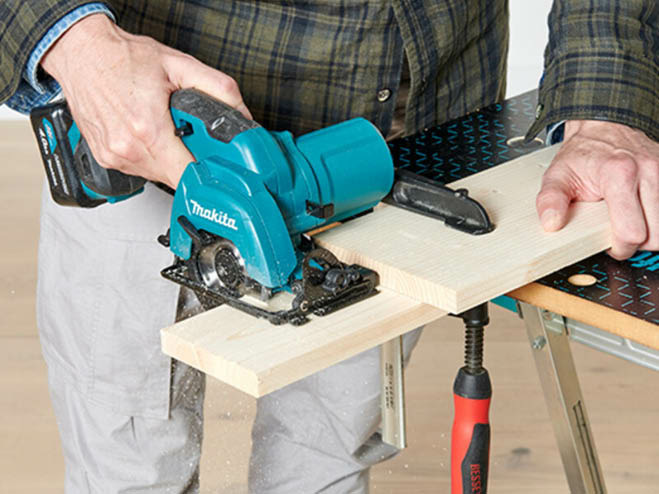 Mit einer Handkreissäge wird eine Holzplatte zugeschnitten