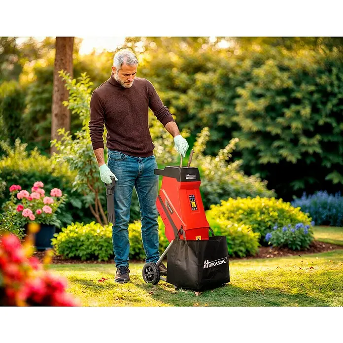 Hurricane Elektro-Messerhäcksler HMH-S-2400 - Max. Aststärke: 4,5 cm, 2.400 W - Ein Mann benutzt einen roten Hurricane Gartenhäcksler mit Fangkorb in einem üppigen Garten.
