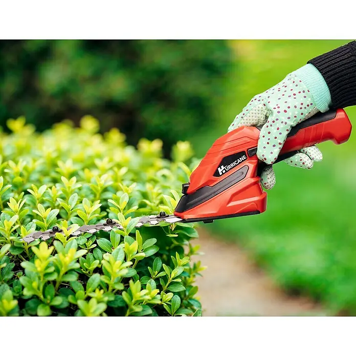 Hurricane Akku-Gras- & Strauchschere HGS-I-55.1 - 3,6 V, Li-Ionen, 1 Akku, Schwertbreite: 9 cm - Eine Hand mit Gartenhandschuh bedient eine rote Hurricane-Heckenschere, um einen kleinen Strauch zu schneiden.