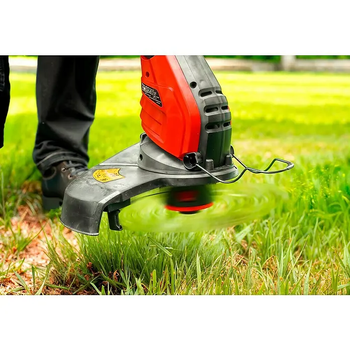 Hurricane Elektro-Rasentrimmer HERT-I-4530 - 450 W, Schnittbreite Faden: 30 cm - Ein Rasentrimmer in Aktion, der Gras schneidet. Das rote und schwarze Gartengerät ist auf einem grünen Rasen im Einsatz.