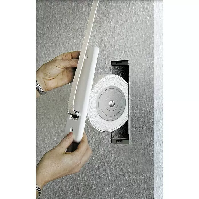 Schellenberg Recogedor de cinta de persiana Maxi - Distancia entre orificios: 135 mm, Anchura de la correa: 23 mm, Máx. Longitud de la cinta: 5,6 m - Manos instalan un recogedor de persiana blanco con cinta textil en un hueco de pared.