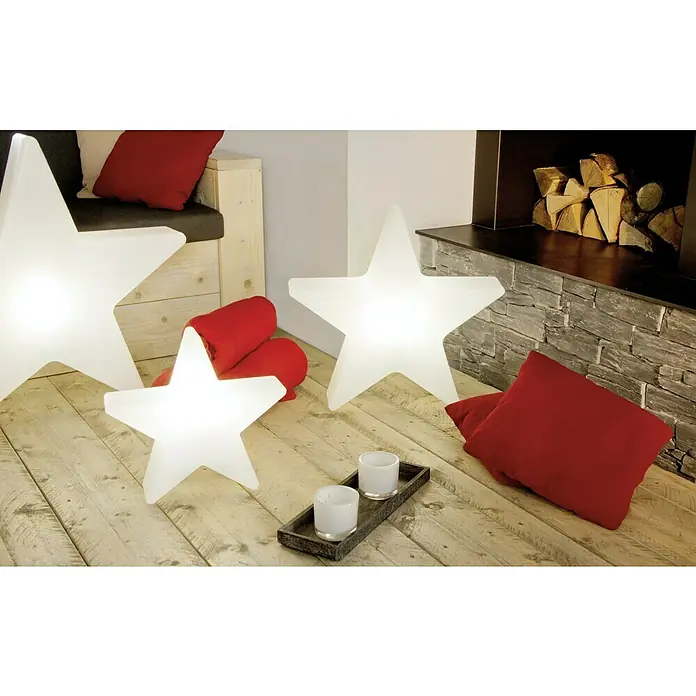 8 Seasons Design Shining LED-Stern Star Mini - 6 W, Weiß, Durchmesser: 40 cm - Eine gemütliche Szene mit leuchtenden Sternleuchten, roten Kissen und Kerzen auf einem Holzboden, die eine warme Atmosphäre schaffen.