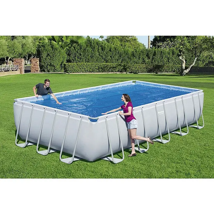Bestway Solarabdeckplane - L x B: 336 x 703 cm, Material: Kunststoff - Rechteckiger Bestway Power Steel Pool mit Abdeckung, umgeben von zwei Personen auf einem Rasen mit Büschen und Bäumen im Hintergrund.
