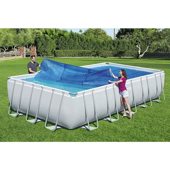 Bestway Solarabdeckplane - L x B: 336 x 703 cm, Material: Kunststoff - Ein rechteckiger Bestway-Pool wird mit einer blauen Poolabdeckung abgedeckt, die von zwei Personen gehalten wird.