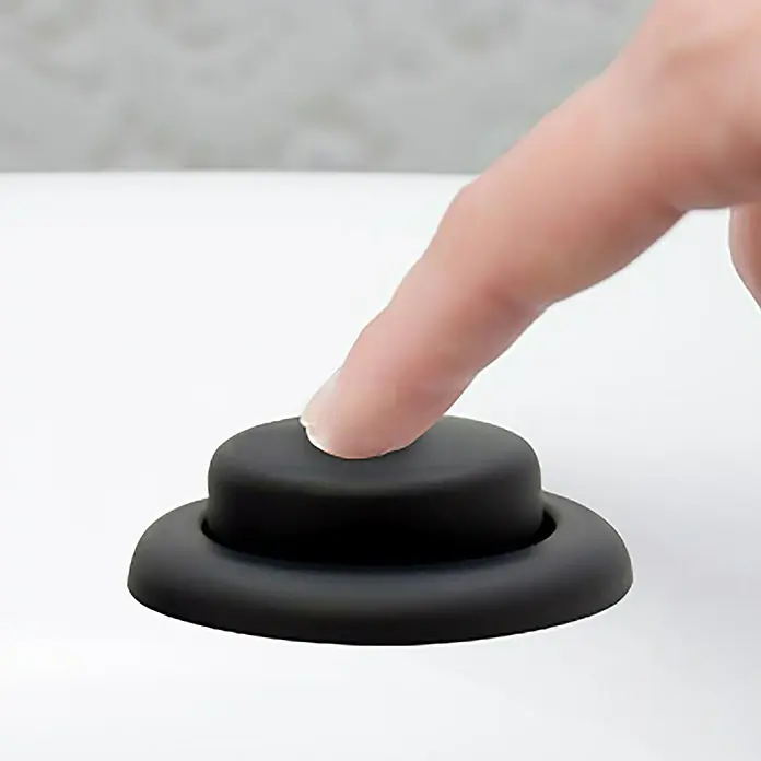 Pulsador de descarga simple - Negro - Primer plano de un dedo presionando un botón negro sobre una superficie blanca, destacando la facilidad de uso del producto.