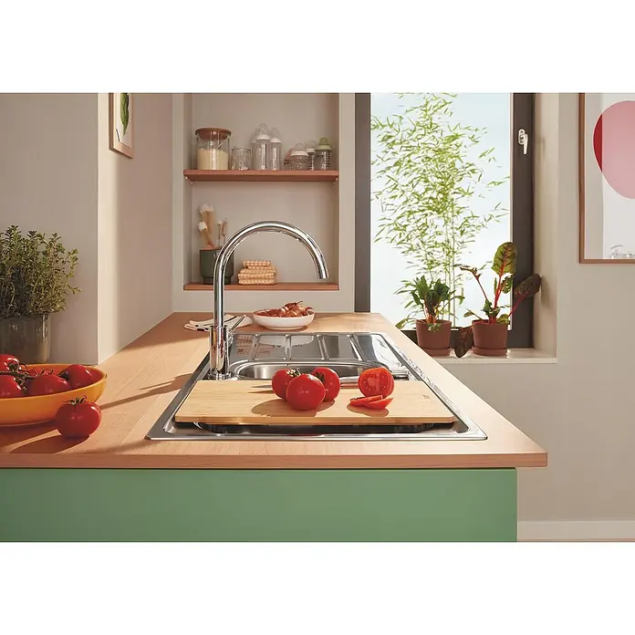 Grohe Grifo de cocina Start Edge - Cromo, Brillante - La imagen muestra un fregadero de cocina con una tabla de cortar y algunos tomates. Al fondo, hay una ventana con plantas.