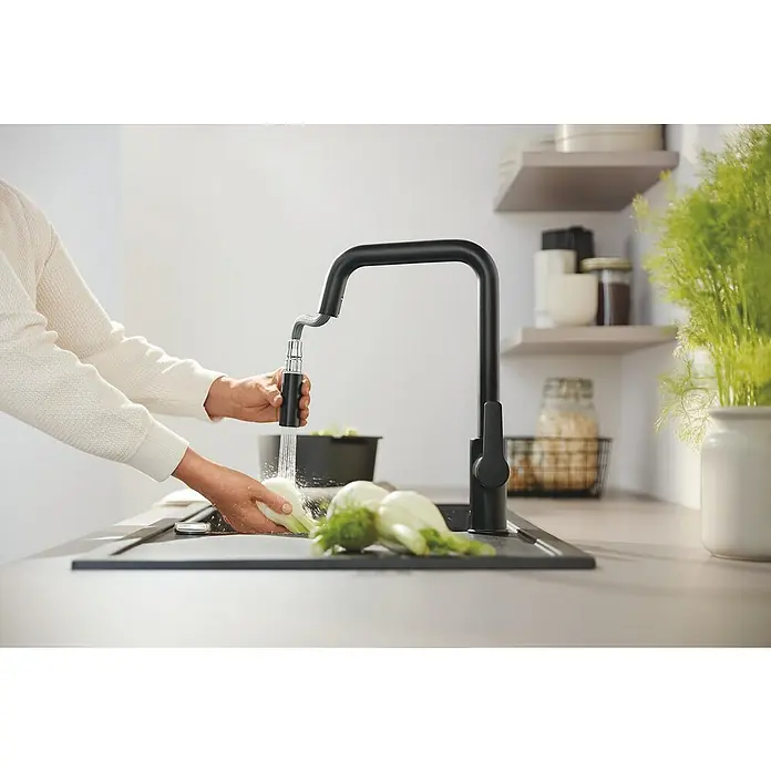 Grohe Grifo de cocina Start - Negro, Mate - Grifo de cocina negro con rociador extraíble, usado por una persona para lavar verduras.