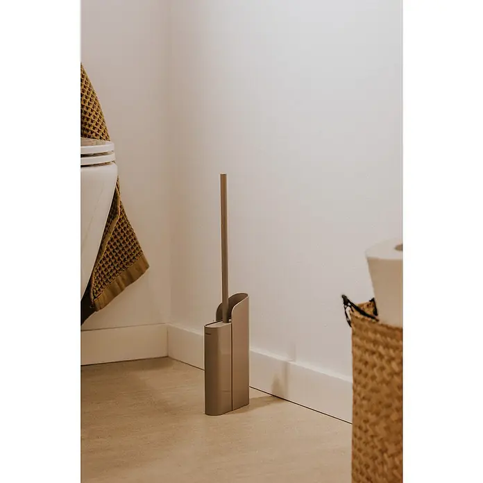 Cosmic Escobillero de suelo y pared Slim - Silicona, Sand - Elegante escobilla de baño color taupe con soporte colocado junto al inodoro. Su diseño elegante complementa la decoración moderna del baño.