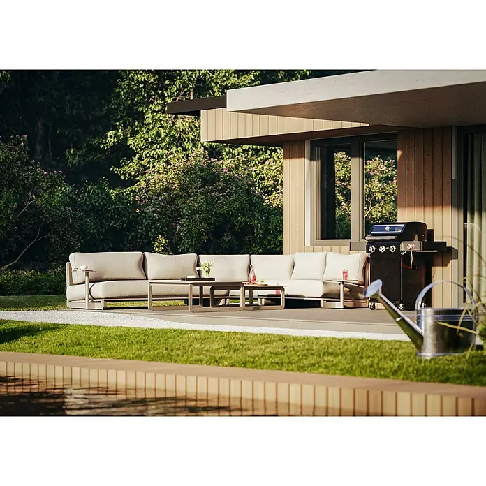 Loungemöbel-Set - 7 -tlg., Aluminium, Polyester, Dust Nature - Outdoor-Szene mit grauer Lounge-Garnitur, Couchtisch, Grill und Gießkanne auf einer Terrasse mit Blick auf einen Garten.