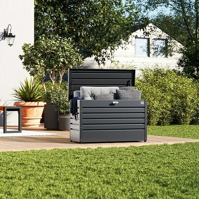 Biohort FreizeitBox Gartenbox 100 - L x B x H: 101 x 46 x 61 cm, Dunkelgrau Metallic, Stahl - Eine stilvolle, graue Gartenbox auf einer Holzterrasse, die ideal zur Aufbewahrung von Kissen und Gartenutensilien ist.
