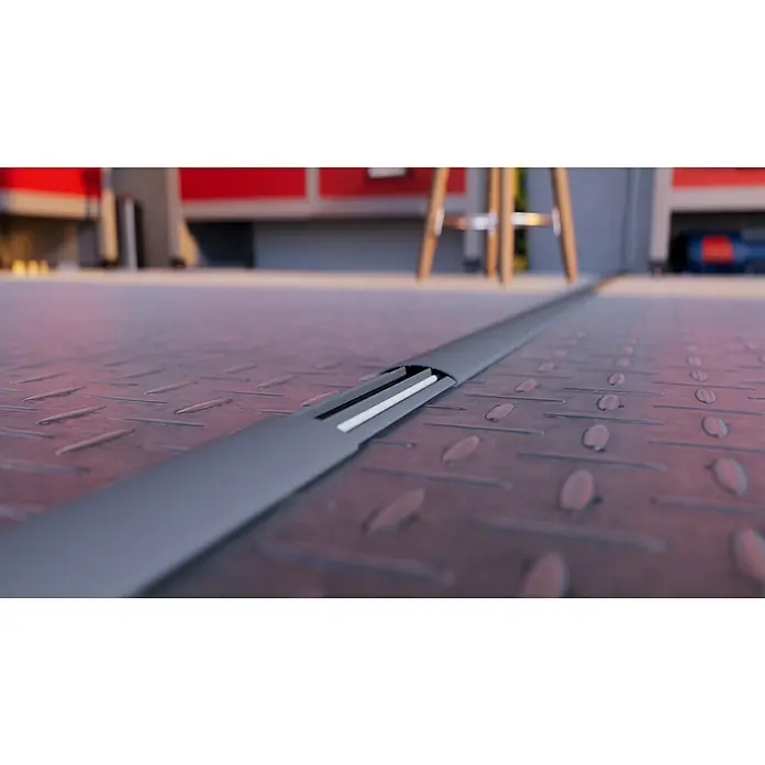 Aufbodenkanal - Steingrau, PVC, L x B x H: 2 m x 50 mm x 12 mm - Nahaufnahme einer grauen Kabelabdeckung auf einem robusten Metallboden, ideal zum Schutz von Kabeln in Werkstätten oder Garagen.