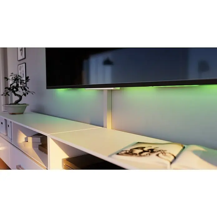 OBO Kabelkanal - 2 m x 40 mm x 40 mm, Lichtgrau - Nahaufnahme eines Fernsehers mit grüner Hintergrundbeleuchtung, montiert über einem weißen Medienschrank mit Dekorationen.
