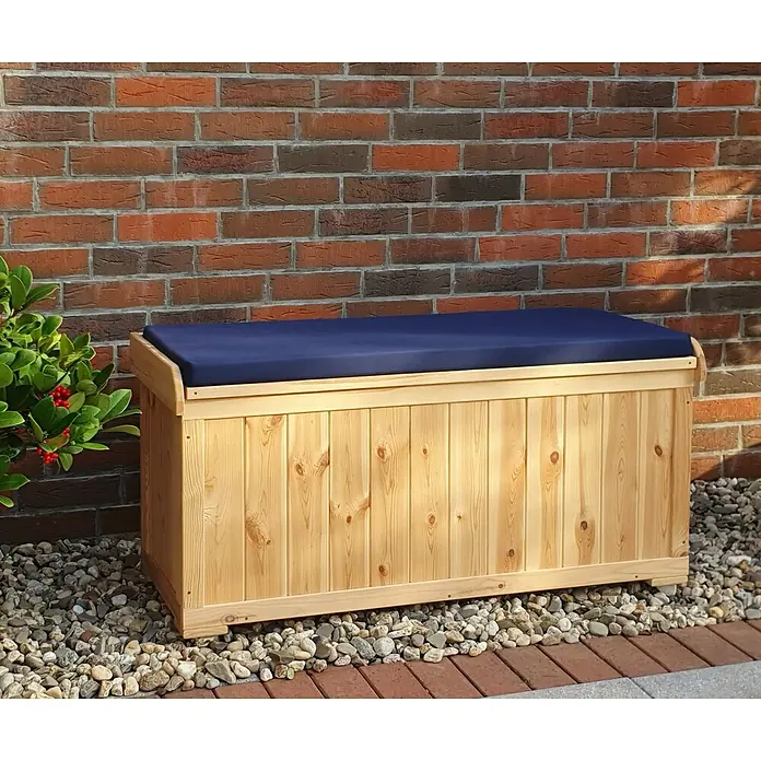 Promadino Gartenbox - L x B x H: 51 x 120 x 56 cm, Holz - Gartenbanktruhe aus Kiefernholz mit marineblauem Kissen vor einer Ziegelmauer.