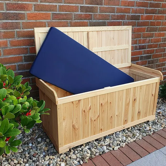 Promadino Gartenbox - L x B x H: 51 x 120 x 56 cm, Holz - Holztruhe mit blauem Sitzkissen steht auf Kies vor einer Backsteinmauer. Ideal zur Aufbewahrung und als Sitzgelegenheit im Garten.