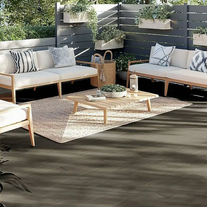 Dioco Tablón para terraza WPC Duratech - L x An x Es: 220 x 14,2 x 2,3 cm, Arena/Gris, 1 ud. - Patio acogedor con sofás de colores claros, una mesa de madera sobre una alfombra y maceteros decorativos contra una pared de madera gris.