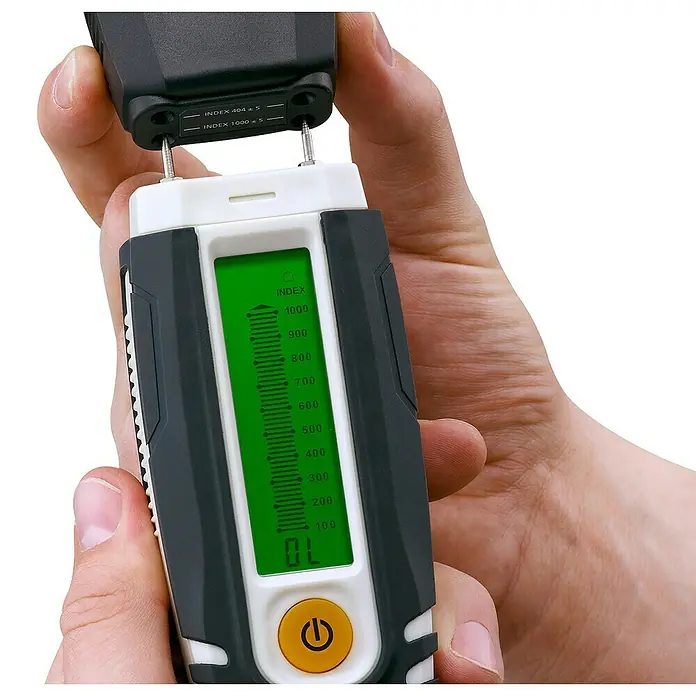 Laserliner Feuchtigkeitsmessgerät Compact - Geeignet für: Baumaterialien/Holz - Hand hält schwarz-weißes Feuchtigkeitsmessgerät. Schutzkappe entfernt zeigt Messstifte. Grünes Display zeigt 'OL' und Indexskala; gelber Ein/Aus-Knopf.