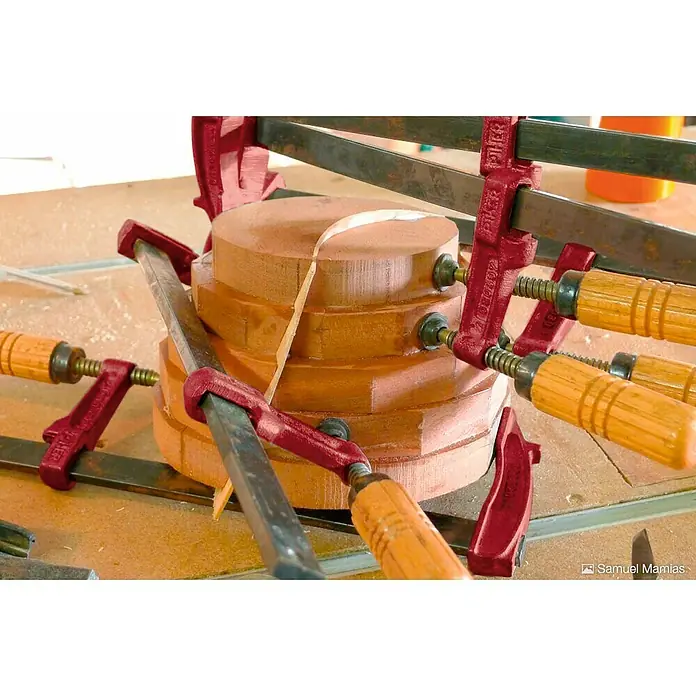 Piher Sargento MM-30 - Anchura de sujeción: 300 mm, Fuerza de tensión: 4.000 N, Apertura máxima: 70 mm - Piezas de madera se sujetan con sargentos rojos en un banco de trabajo, creando un proyecto de carpintería sólido y encolado.