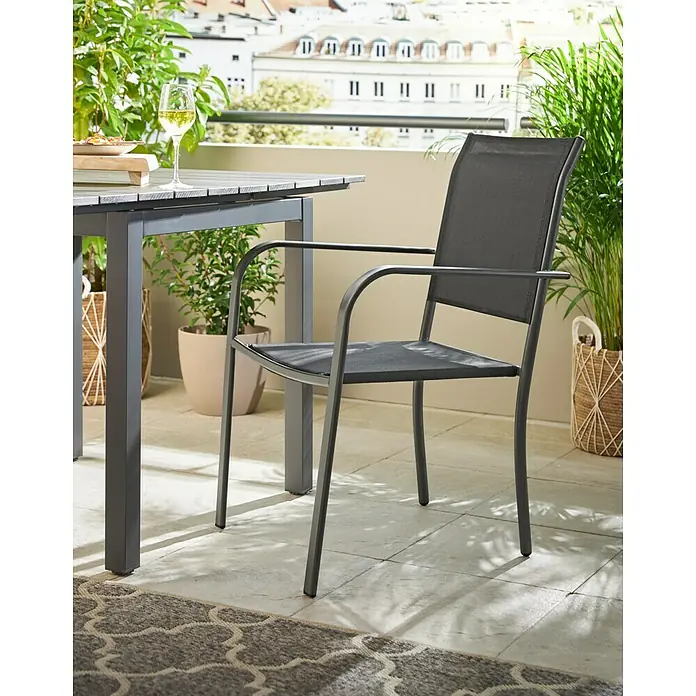 Stapelstuhl - Stahl, Textil, Stapelbar, Night-Grey, B x T x H: 56 x 66 x 86 cm - Hier ist ein grauer Terrassenstuhl mit Armlehnen, der zu einem Esstisch gehört, umgeben von Topfpflanzen und einem Teppich.