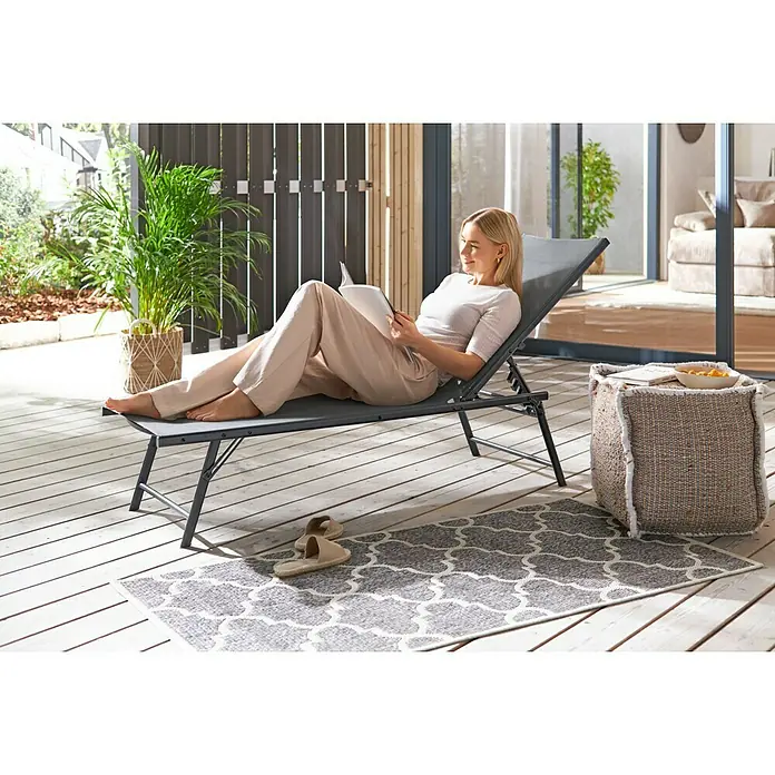 Gartenliege - L x B x H: 181 x 54,5 x 33,5 cm, Dunkelgrau, Stahl, Klappbar - Frau entspannt auf einer grauen Sonnenliege im Freien und liest ein Buch. Entspannen Sie sich stilvoll auf dieser Liege.
