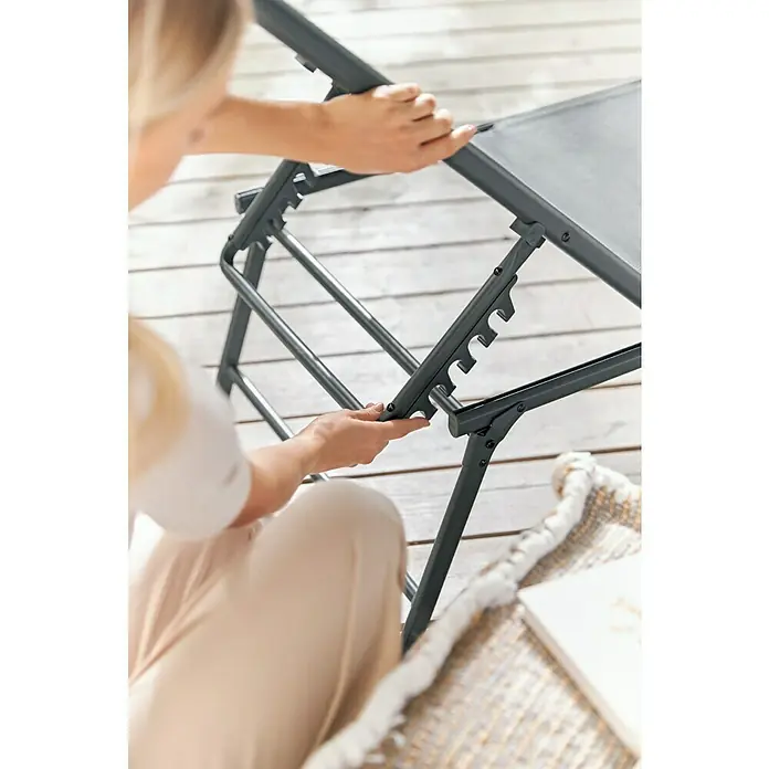 Gartenliege - L x B x H: 181 x 54,5 x 33,5 cm, Dunkelgrau, Stahl, Klappbar - Detailaufnahme eines verstellbaren, grauen Liegestuhls, der auf einem hellen Holzboden steht. Eine Person passt die Position des Stuhls an.