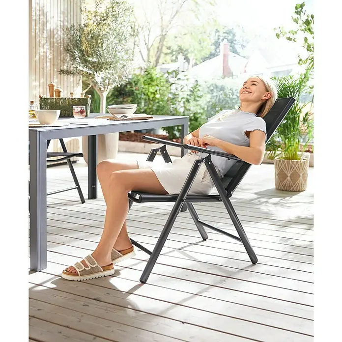 Garten-Positionssessel Maja - Aluminium, Textilen, Rückenlehne verstellbar, Anthrazit/Schwarz, B x T x H: 55 x 68 x 106 cm - Eine Frau entspannt auf einem bequemen Gartensessel auf einer sonnigen Terrasse. Das perfekte Möbelstück zum Entspannen im Freien.