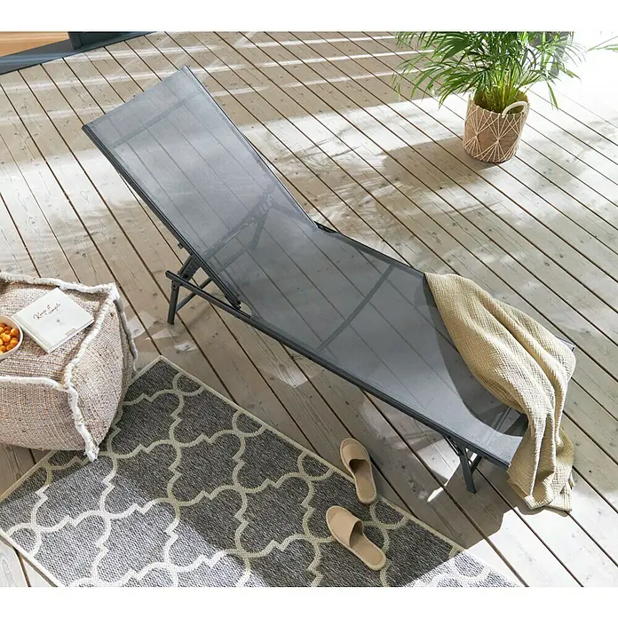 Gartenliege - L x B x H: 181 x 54,5 x 33,5 cm, Dunkelgrau, Stahl, Klappbar - Graue Sonnenliege aus Stoff und Metall mit Handtuch auf einer Holzterrasse mit Teppich, Beistelltisch und Zimmerpflanze.
