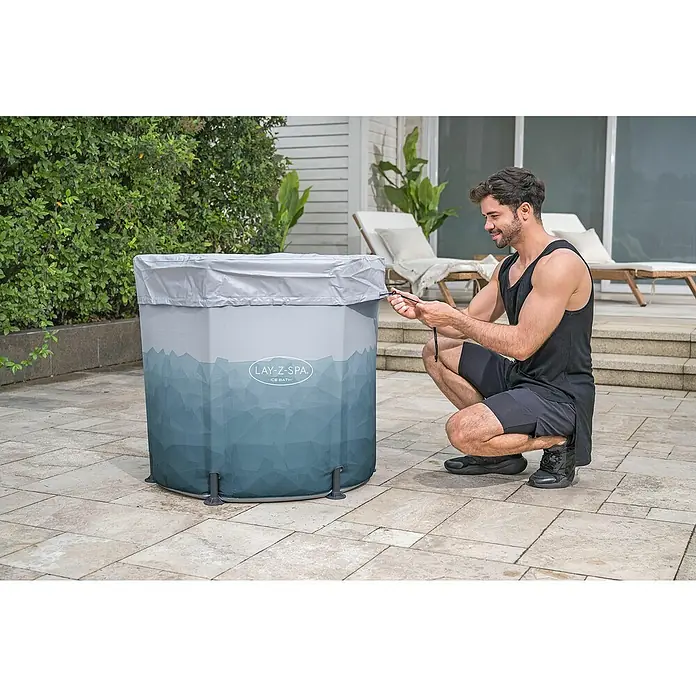Bestway Lay-Z-Spa Eisbad Glacial Dip - 253 l, Ø x H: 90 x 80 cm - Ein Mann hockt neben einem Lay-Z-Spa Ice Bath und befestigt die Abdeckung. Er scheint mit dem Produkt zufrieden zu sein.