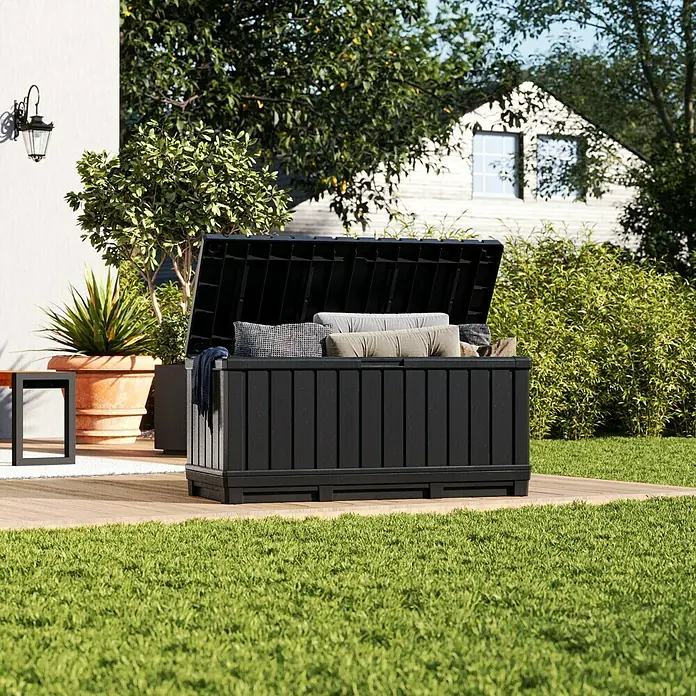 Keter Garten-Aufbewahrungsbox Kentwood - L x B x H: 128 x 53,6 x 59 cm, Kunststoff - Schwarze Gartenbox mit geöffnetem Deckel, gefüllt mit Kissen und Decken, steht auf einer Holzterrasse im Garten.