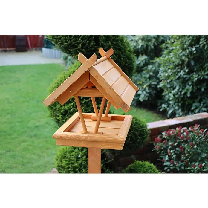 Promadino Vogelhaus Rhön - 42 x 36 x 38 cm, Holz, Braun, Ausstattung: Ohne Vogelhausständer - Hölzernes Vogelhaus mit geneigtem Dach und quadratischer Plattform, umgeben von üppigem Grün in einem Garten.