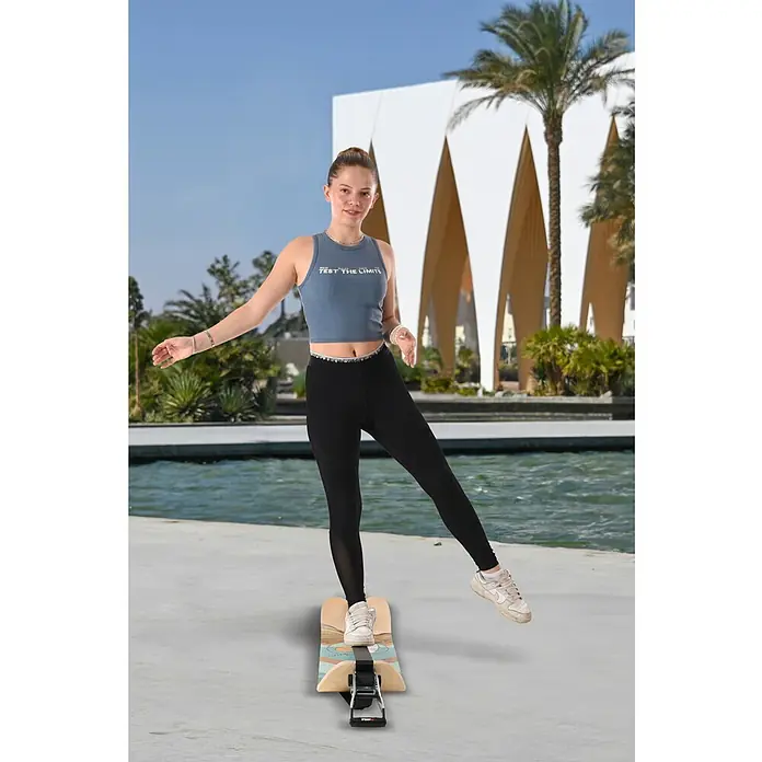 F2 Balance Board Surfline - L x B: 105 x 27,5 cm - Eine Frau balanciert auf einem Balance Board vor einem modernen Gebäude und Palmen. Sie trägt Sportkleidung.