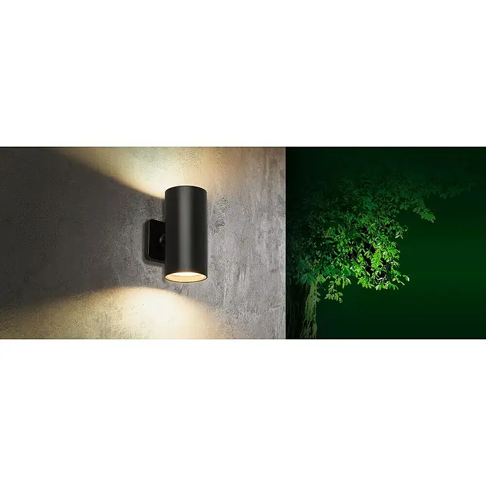Starlux Akku-Wandleuchte Avio - 2,6 W, 7,1 x 5,3 x 11 cm, IP44, Schwarz - Eine zylindrische Außenwandleuchte in Schwarz strahlt warmes Licht auf eine strukturierte Wand, während im Hintergrund ein Baum sichtbar ist.