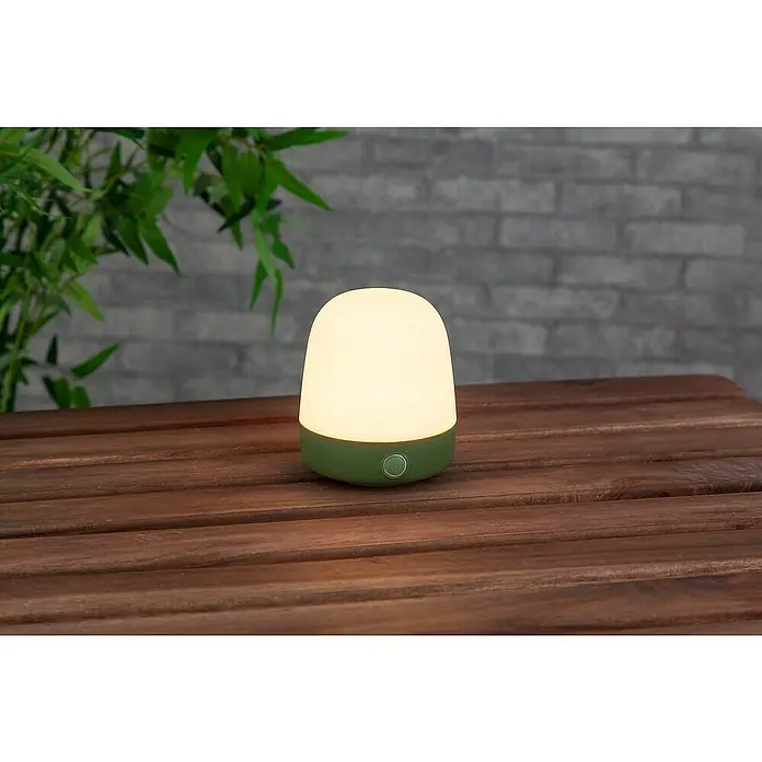 Starlux Akku-Tischleuchte Mini - L x B x H: 10 x 10 x 12 cm, Matcha Green, RGBW, 0,3 W, IP44 - Eine Nahaufnahme einer grün-weißen Nachtlampe auf einem Holztisch mit verschwommenem Hintergrund, die ein warmes, sanftes Licht ausstrahlt.