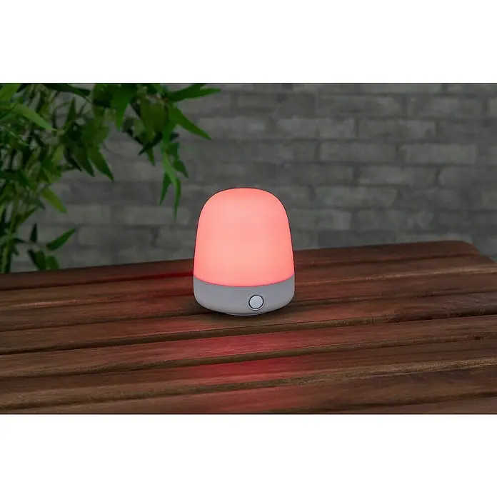 Starlux Akku-Tischleuchte Mini - L x B x H: 10 x 10 x 12 cm, Beige, RGBW, 0,3 W, IP44 - Nahaufnahme einer Nachttischlampe mit sanftem, rotem Licht auf einem Holztisch. Ideal für eine beruhigende Atmosphäre im Schlafzimmer.