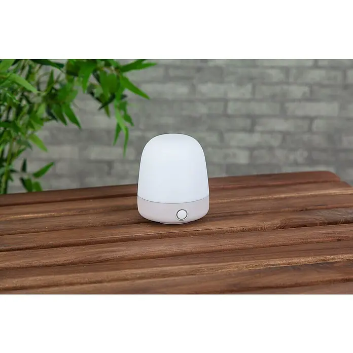Starlux Akku-Tischleuchte Mini - L x B x H: 10 x 10 x 12 cm, Beige, RGBW, 0,3 W, IP44 - Nahaufnahme einer Nachttischlampe mit warmweissem Licht auf einem Holztisch, ideal für sanfte Beleuchtung im Schlafzimmer.