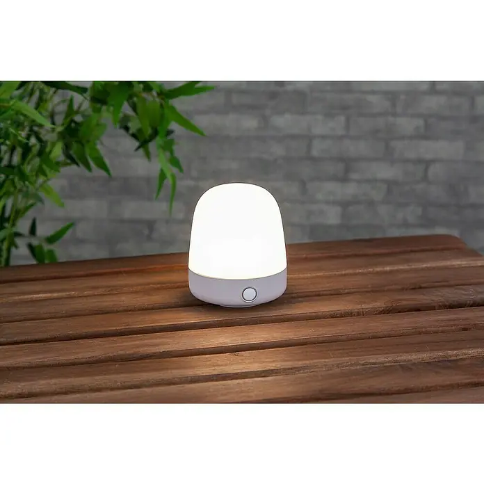 Starlux Akku-Tischleuchte Mini - L x B x H: 10 x 10 x 12 cm, Beige, RGBW, 0,3 W, IP44 - Nahaufnahme einer kleinen, eingeschalteten Tischleuchte auf einer Holzoberfläche, ideal als Nachtlicht oder für stimmungsvolle Beleuchtung.