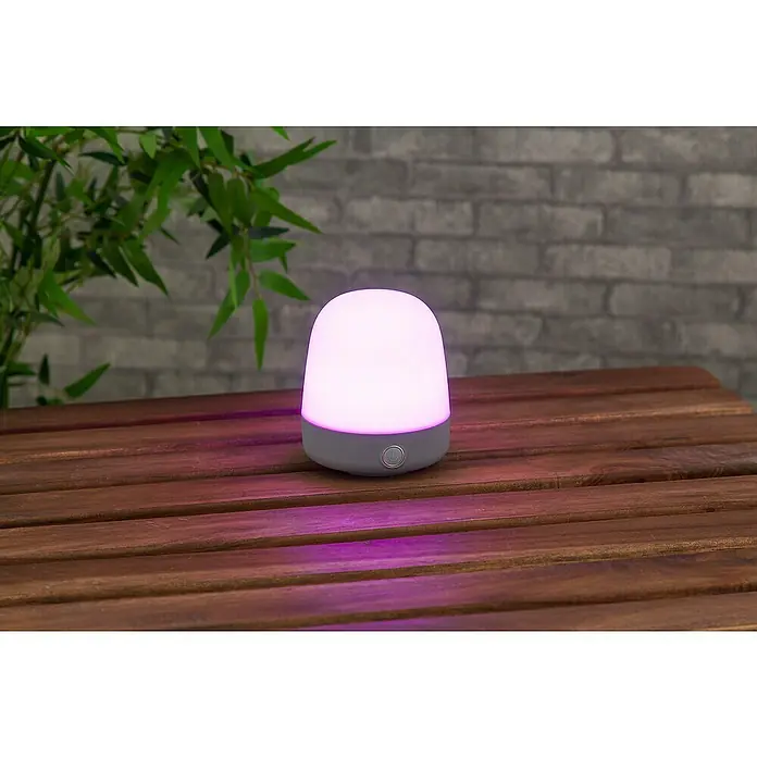Starlux Akku-Tischleuchte Mini - L x B x H: 10 x 10 x 12 cm, Light Grey, RGBW, 0,3 W, IP44 - Nahaufnahme einer stimmungsvollen LED-Tischleuchte, die ein sanftes, farbiges Licht auf eine Holzoberfläche wirft, ideal für gemütliche Abende.