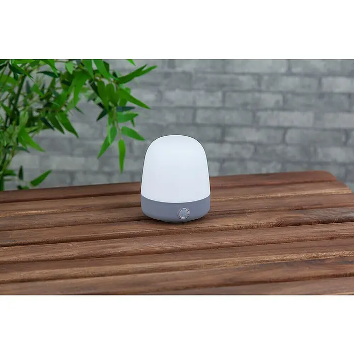 Starlux Akku-Tischleuchte Mini - L x B x H: 10 x 10 x 12 cm, Light Grey, RGBW, 0,3 W, IP44 - Eine graue und weiße kabellose tragbare Nachttischlampe steht auf einem Holztisch. Das sanfte Licht sorgt für eine entspannende Atmosphäre.