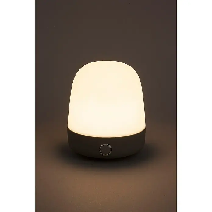 Starlux Akku-Tischleuchte Mini - L x B x H: 10 x 10 x 12 cm, Light Grey, RGBW, 0,3 W, IP44 - Nahaufnahme einer Tischleuchte mit grauem Sockel und weißem Schirm, die ein warmes Licht ausstrahlt.