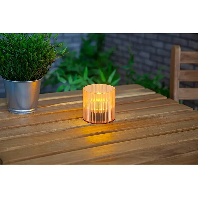 BAUHAUS Solar-Dekoleuchte Teelicht - 0,6 W, Mango, IP44 - Dekorative Tischleuchte im Freien, ein zylindrisches Design mit warmer Beleuchtung, neben einem grünen Topf, auf einem Holztisch für eine gemütliche Atmosphäre.