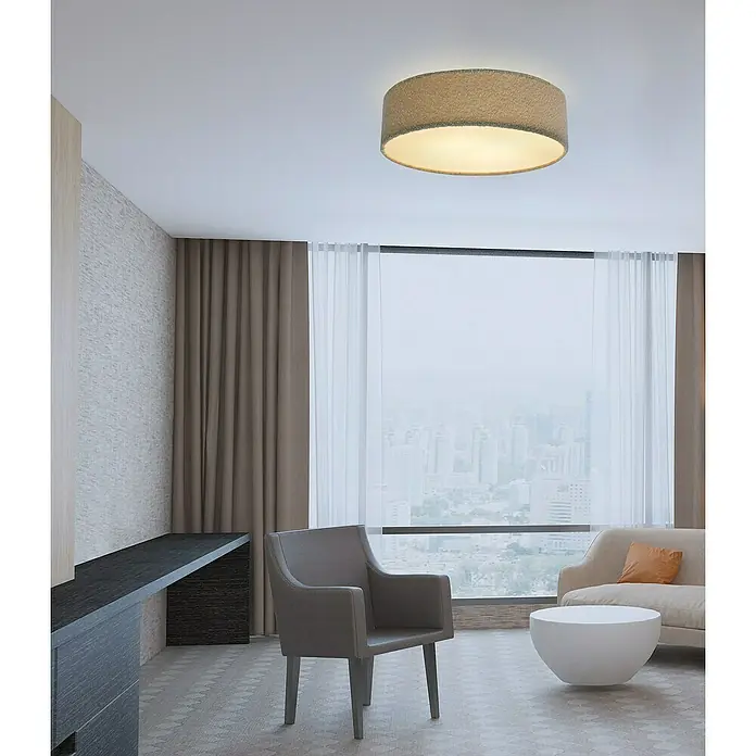 Tween Light Deckenleuchte rund Bouclé-Stoff - Taupe, E27 - Ein modernes Wohnzimmer mit einer runden Deckenleuchte, einem Sessel, einem Tisch und großen Fenstern mit Stadtblick. Die Leuchte ist ein zentrales Element.